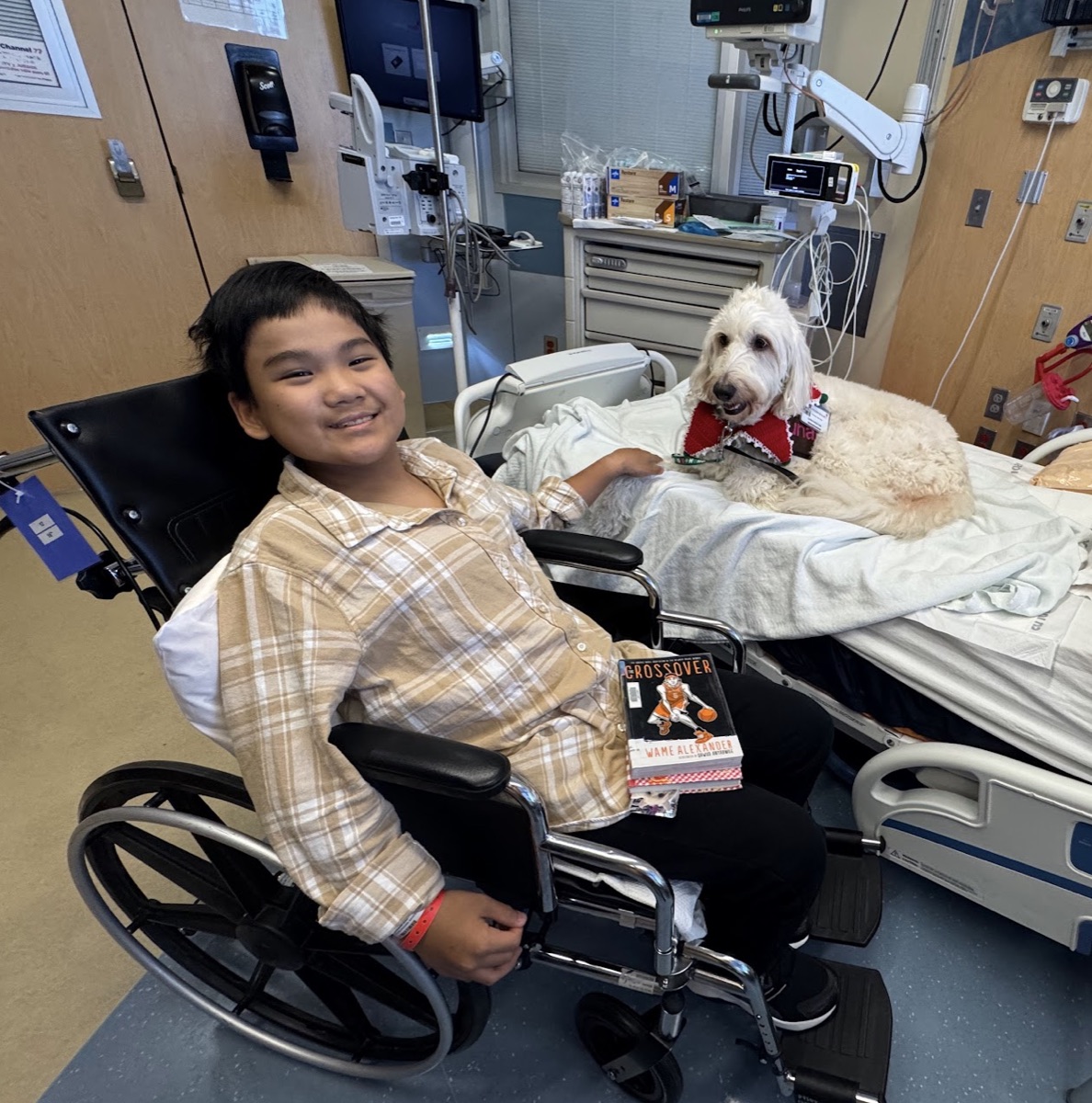 Ryle in wheelchair with therapy dog, smiling